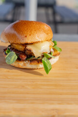 Gros plan sur un hamburger fait maison avec du fromage fondant, un steak et de la salade, le tout présentés sur une planche en bois.