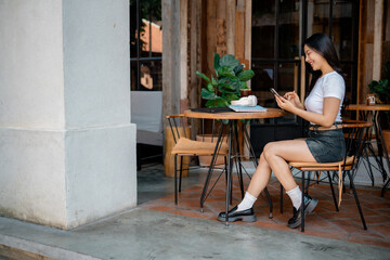 Young Asian Woman Using Smartphone in Outdoor Cafe, Enjoying Coffee and Relaxing