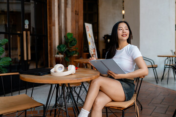 Young asian freelancer woman holding notebook working remotely at cafe