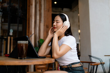 Young Asian woman enjoying music with headphones in a cafe