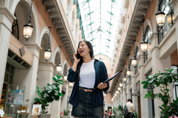 Young businesswoman talking on phone and holding folder in a shopping mall