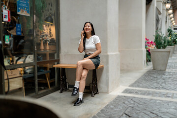 Young woman making a phone call sitting on a bench outside a shop