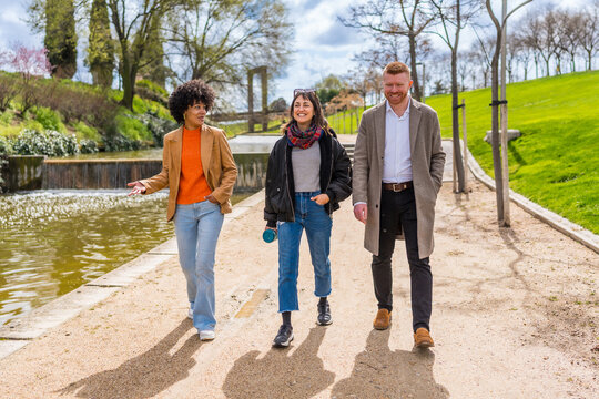 Three colleagues walking and talking in a park near a pond