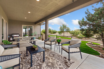 An outdoor patio with a cozy rug, chairs, tables, and a grill