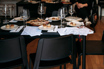 Empty chairs surround a wine workshop table with tasting cards, food samples, and glasses ready for participants. Wine workshop, pre-event setup, tasting preparation, hospitality training