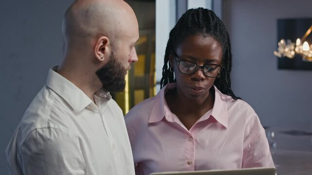 Medium shot of bicultural businesspeople using laptop and communicating while working at modern office