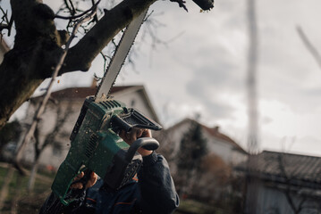 Gardener cutting tree branch with chainsaw in residential area
