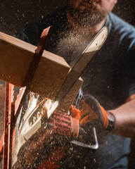 Worker uses a chainsaw to cut a plank into two pieces while working