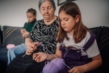 Grandmother teaching granddaughter knitting skills on sofa