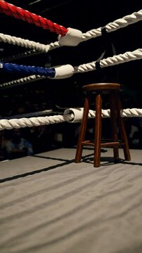 Empty wooden stool in corner of boxing ring, ropes around, quiet anticipation before boxing match