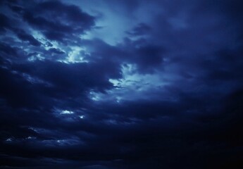 Obraz premium Dark Blue Clouds Rolling Across the Sky with Mysterious Light Peering Through