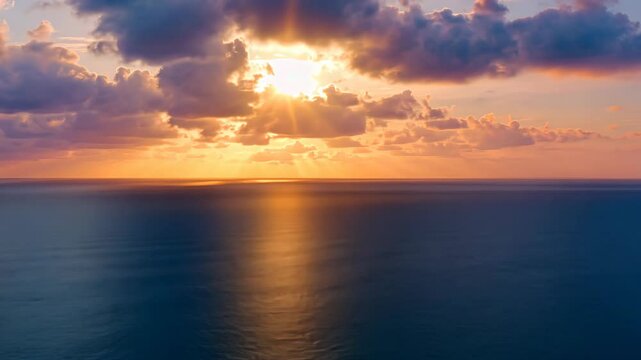 Dramatic seascape view with golden sun rays piercing through clouds at sunset over tranquil dark blue ocean surface