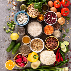 Large set of balanced nutrition products on gray concrete background, top view. Vegetables, fruits, nuts, grains, olive oil, green herbs.
