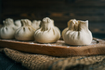 Close-up of raw khinkali dumplings arranged on a floured wooden cutting board, ready for cooking