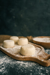 Raw dough pieces on a floured wooden board with one placed on a spoon, ready for baking on a rustic kitchen table