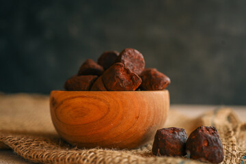 Rustic wooden bowl filled with rich cocoa-dusted chocolate truffles on burlap fabric with a dark moody background