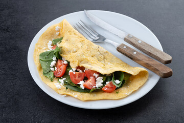 Stuffed omelette with tomatoes and spinach on black stone