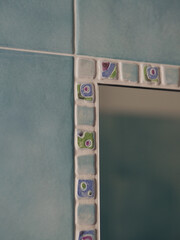Obraz premium Mosaic-Framed Mirror on Blue Tiled Wall, Vertical Close-Up of Italian Bathroom Detail