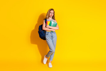 Confident young student wearing casual fashion with book and backpack on yellow background,...