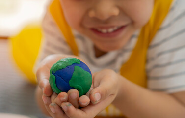 Happy little boy playing with modeling clay and he molded it to a globe