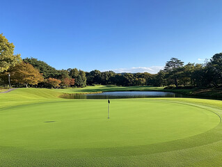 Obraz premium eye-level view of a pristine putting green on a Japanese golf course, smooth manicured surface with visible flagstick, surrounded by lush fairway, distant trees, and a calm water hazard