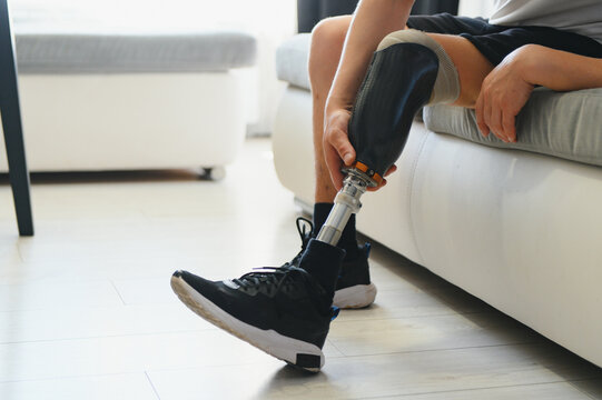Man amputee with prosthetic leg disability on above knee transfemoral leg prosthesis wearing shoe sitting on sofa, close up. People with amputation disabilities everyday life concept