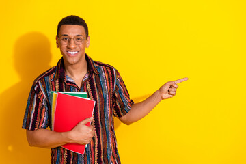 Smiling young man with book on a vibrant yellow background making a positive gesture, suitable for...