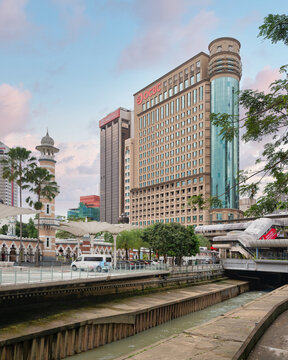 Kuala Lumpur, Malaysia - Feb. 21, 2025: Minaret of Sultan Abdul Samad Jamek Mosque, next to CIMB and OCBC contemporary bank buildings, with lush greenery and calm waterway of the River of Life