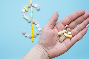 Cost of medication: pills forming dollar sign on blue background with hand holding various tablets