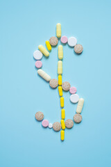 Pills arranged in dollar sign symbol on blue background