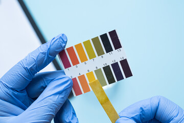 Gloved hands holding ph test strip with color scale on blue background. Neutral pH environment.