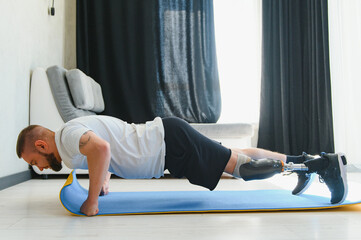 Sporty fit young man amputee with prosthetic leg disability prosthesis doing plank exercise on mat...