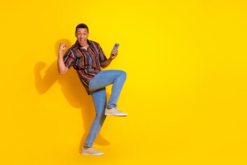 Cheerful young man celebrating success while holding a phone against a bright yellow background