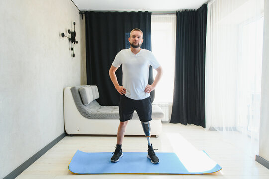 Man amputee with prosthetic leg disability on transfemoral leg prosthesis artificial device making stretching rehabilitation physical exercise at home. People w amputation disabilities everyday life