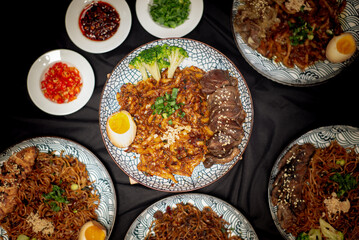 flatlay angle fried udon with chili oil served with beef barbeque and broccoli also with half boiled egg on top. Served on a white and black pattern plate. Portrait angle