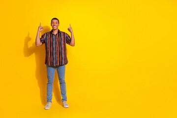 Smiling young man gesturing confidently on a vibrant yellow background while dressed stylishly in a...