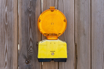 A yellow and black traffic light is hanging on a wooden fence. The light is on and is lit up
