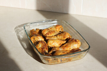 close up of home style crispy roasted chicken legs drumsticks in garlic mayo sauce in a transparent glass cooking dish in kitchen with sunny light background