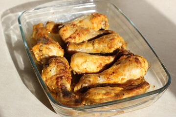 close up of home style crispy roasted chicken legs drumsticks in garlic mayo sauce in a transparent glass cooking dish in kitchen with sunny light background