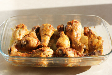 close up of home style crispy roasted chicken legs drumsticks in garlic mayo sauce in a transparent glass cooking dish in kitchen with sunny light background