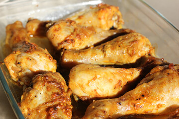 close up of home style crispy roasted chicken legs drumsticks in garlic mayo sauce in a transparent glass cooking dish in kitchen with sunny light background