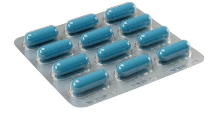 Close up shot of a blister pack containing several blue capsules on a white surface in a studio shot