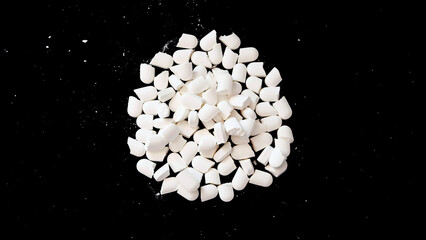 A pile of white supplement tablets, split into half the size. With dark background.
