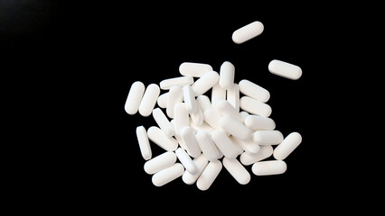 Closeup of a pile of oval white supplement tablets. With black background.