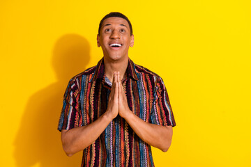 Young cheerful man in a vibrant patterned shirt posing against a bright yellow background...