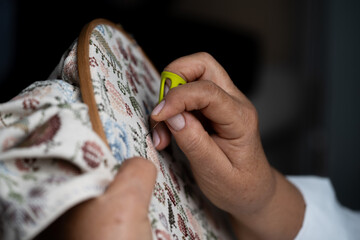 Seamstress embroidering a floral pattern using a needle threader and an embroidery hoop