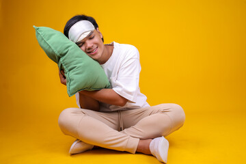 Calm Young Man in Pajamas Sleeping with Pillow While Sitting on Yellow Background