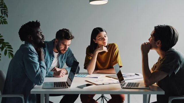 Three diverse colleagues, including an african american man, are engaged in a focused discussion, analyzing charts and brainstorming ideas while seated at a table with laptops and documents