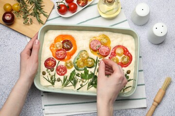 Woman adding thyme to raw focaccia at grey table, top view