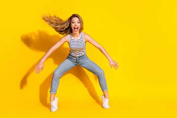 Excited young woman jumping joyfully in casual clothing against a vibrant yellow background